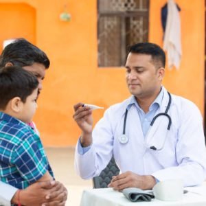 Indian Doctor examine little kid boy patient fever at village with digital thermometer, Father with his son consulting medical person,Rural India healthcare camp concept.